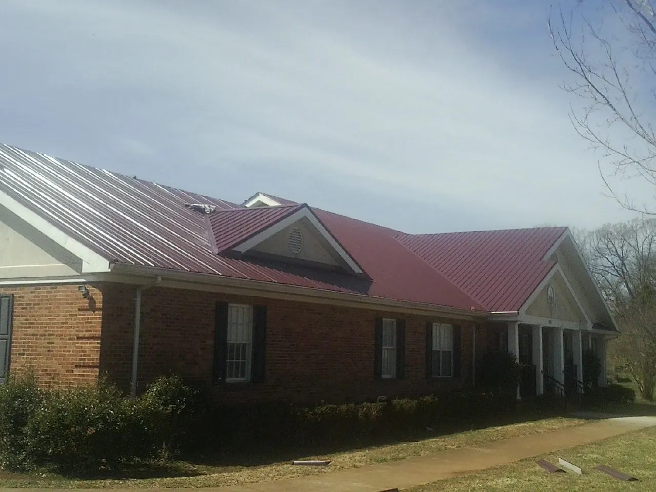 Red metal roof with gabled entries on a long brick building, from a Hail Damage Roof Repair job in Weber City