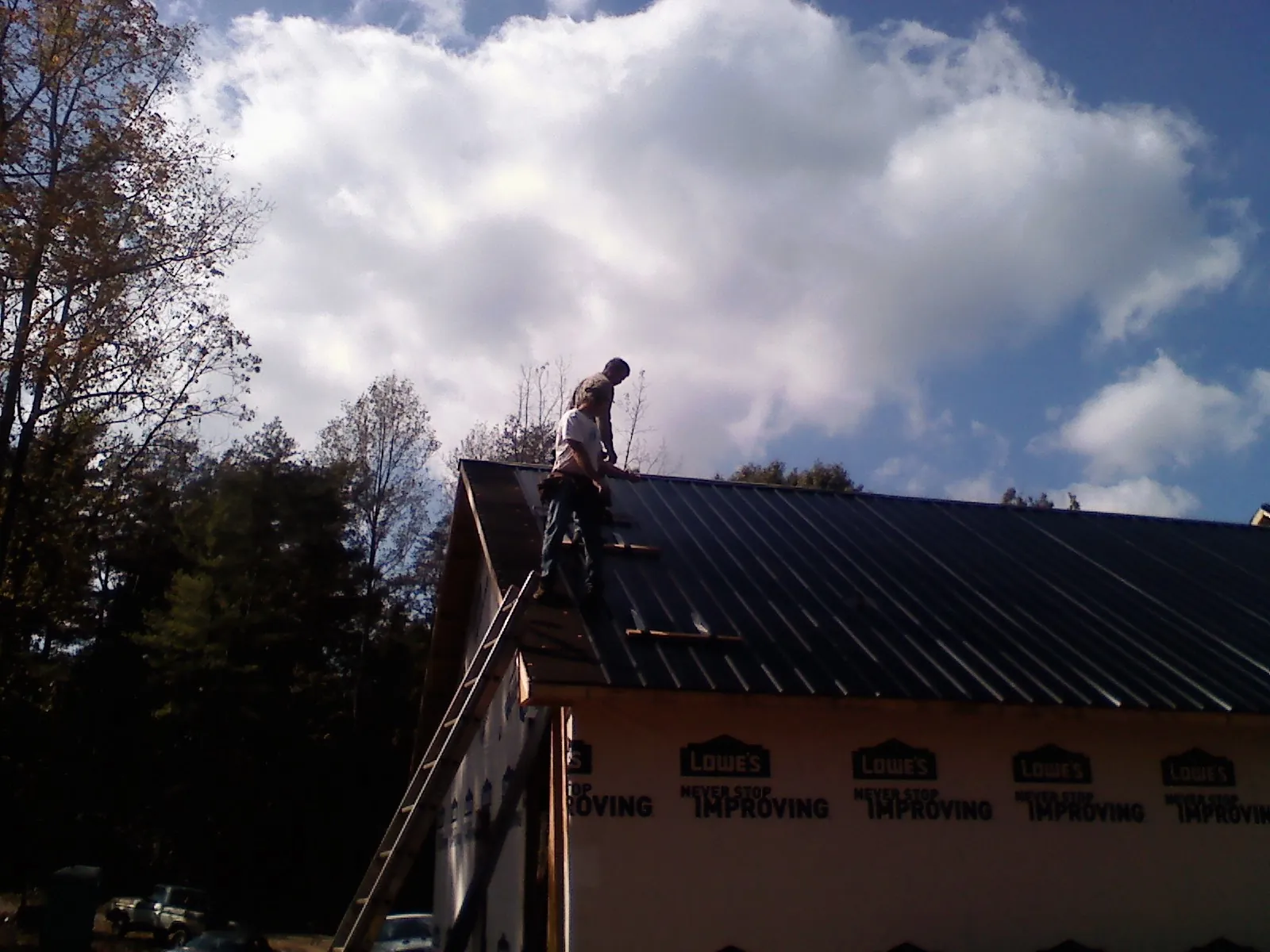 Roofer fastening dark metal panels high against a cloudy sky, from a Roof Inspection job in Weber City