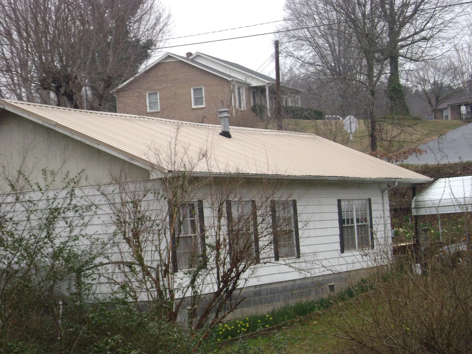 Tan metal roof on a white sided house set into a hillside — Commercial Roofing by Roofing Brothers in Weber City